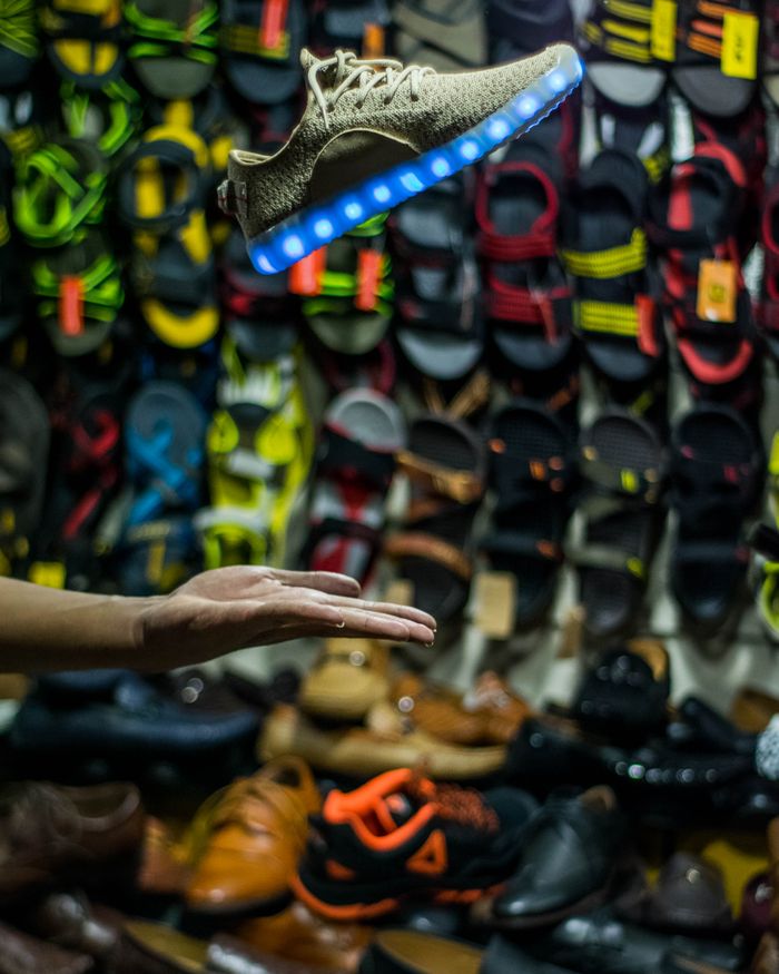 LED-lit shoe tossed above colorful footwear at a Karachi shop stall.