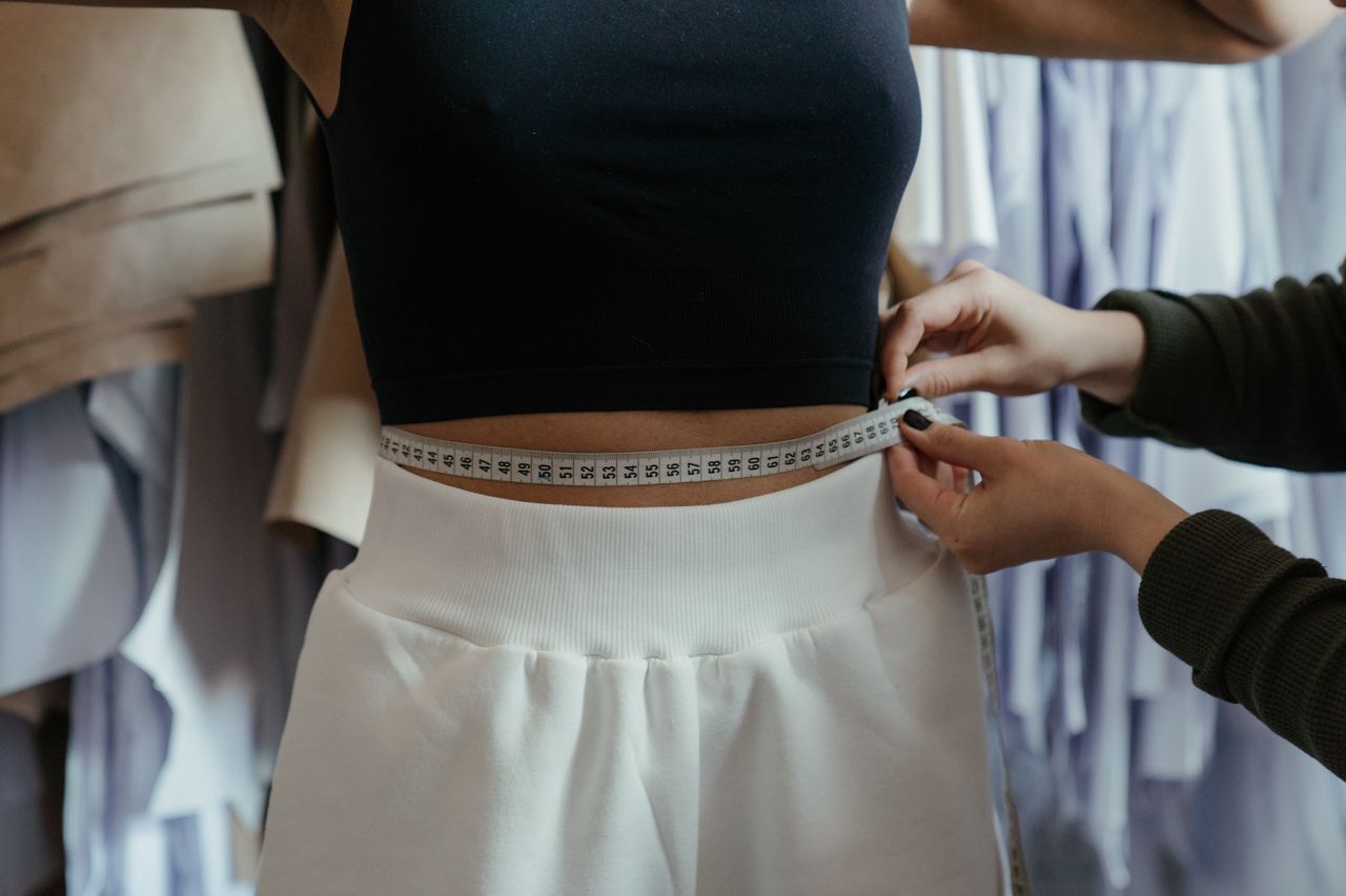 Detailed view of a tailor measuring a client's waist in a clothing workshop, focusing on precision.