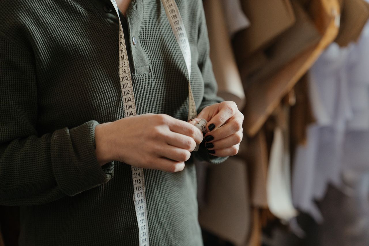 Close-up of a person using a measuring tape in a sewing studio, focusing on patterns and precision.