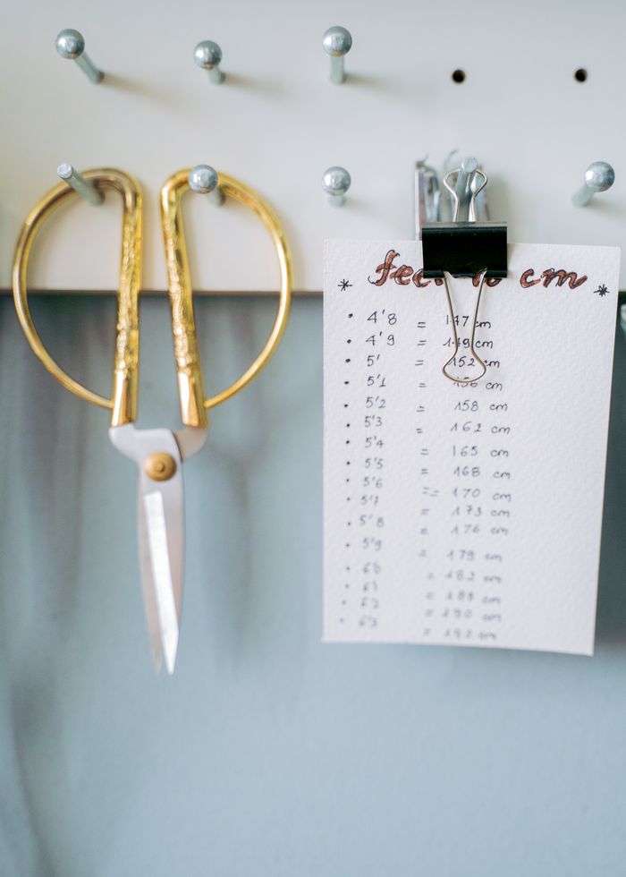 Gold scissors and a conversion chart hang on a pegboard. Ideal for sewing or crafting contexts.