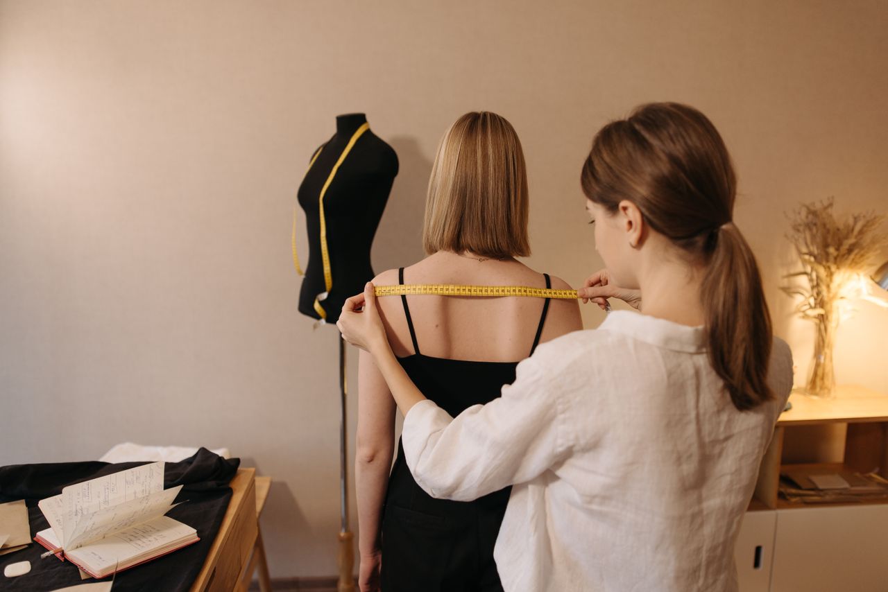 A tailor measuring a woman for a custom fit garment in a sewing workspace.