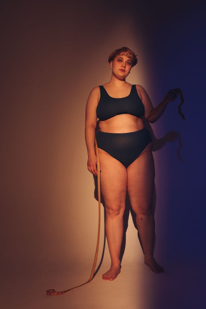 A plus size woman in a minimalist studio showing body confidence with dramatic lighting and shadows.