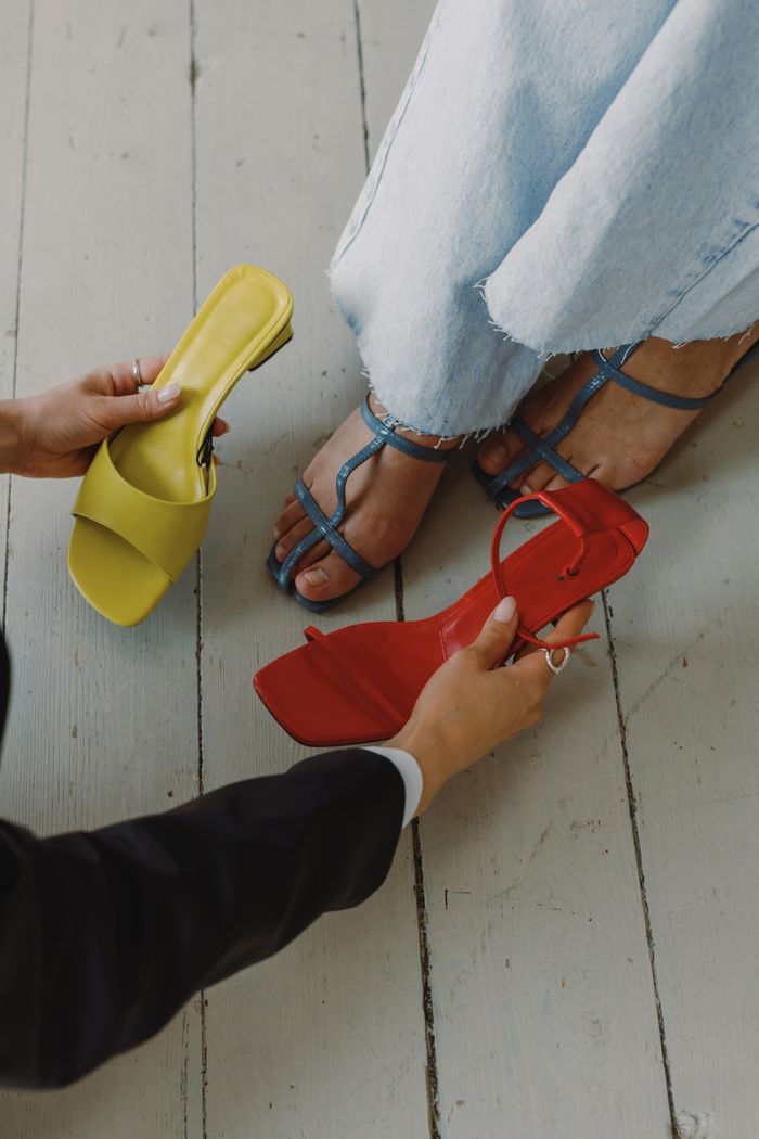 Fashionable footwear selection with hands helping choose shoes on wooden floor.